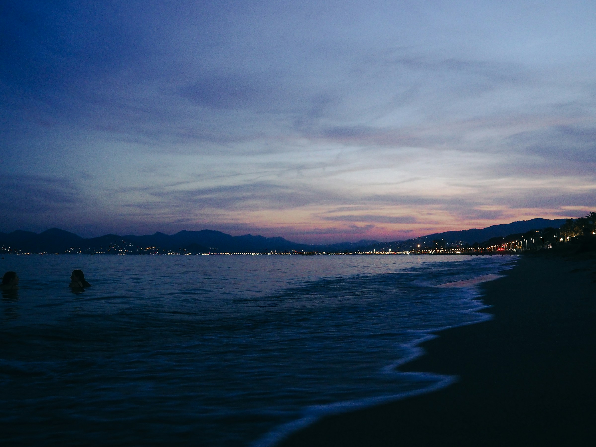A quiet beach at dusk, the shoreline stretching toward distant town lights under a deep twilight sky